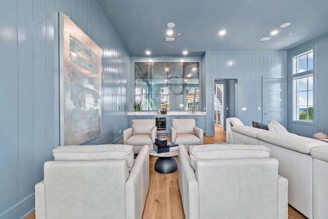 living room with light wood-type flooring, wooden walls, and wine cooler