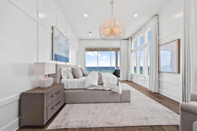 bedroom featuring access to outside, a water view, dark hardwood / wood-style floors, and a notable chandelier