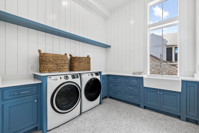 washroom with wooden walls, sink, washing machine and clothes dryer, and cabinets