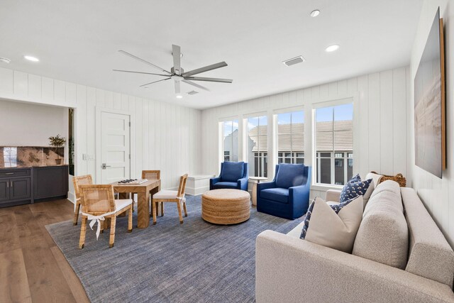 living room with ceiling fan, dark hardwood / wood-style floors, and wood walls