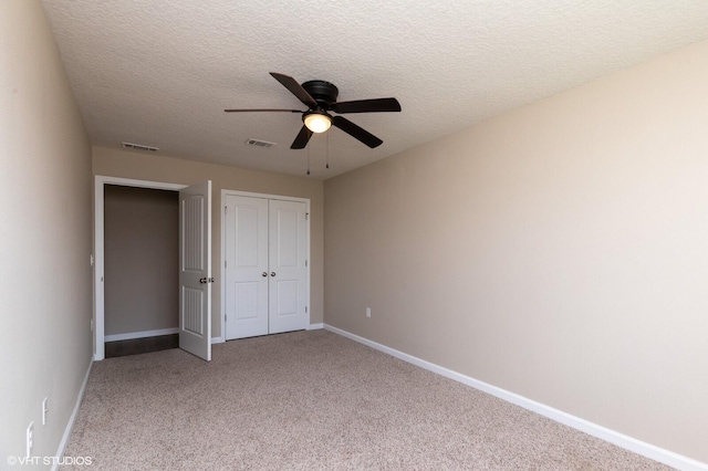 unfurnished bedroom featuring a closet, ceiling fan, light colored carpet, and a textured ceiling