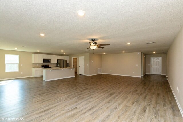 unfurnished living room with a textured ceiling, ceiling fan, light hardwood / wood-style flooring, and sink