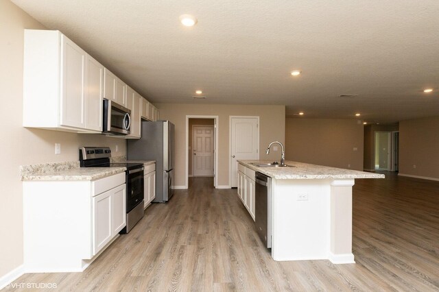 kitchen with white cabinets, an island with sink, sink, appliances with stainless steel finishes, and light hardwood / wood-style floors