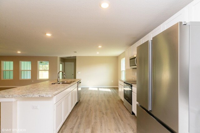 kitchen with appliances with stainless steel finishes, white cabinetry, light hardwood / wood-style flooring, a center island with sink, and sink