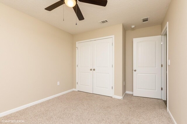 unfurnished bedroom with a closet, ceiling fan, light colored carpet, and a textured ceiling