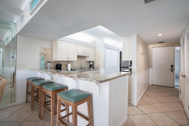 114 Main Sail Dr Unit 137, Miramar Beach, FL 32550 - kitchen with a peninsula, a kitchen breakfast bar, light tile patterned floors, backsplash, and a wainscoted wall