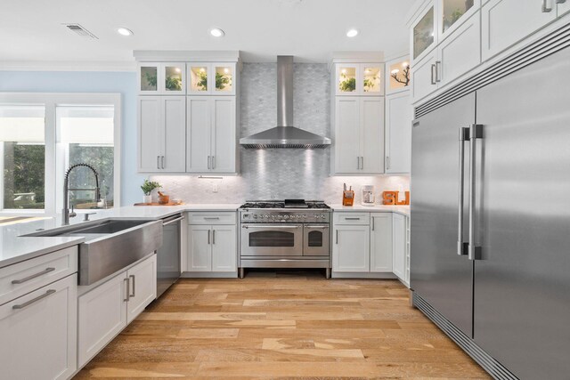 kitchen featuring white cabinets, high quality appliances, and wall chimney range hood