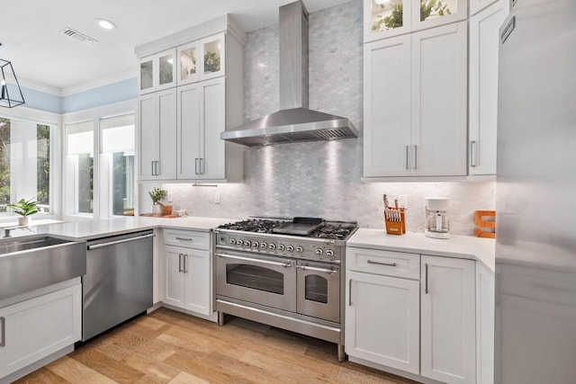 kitchen with light hardwood / wood-style flooring, white cabinets, appliances with stainless steel finishes, and wall chimney range hood