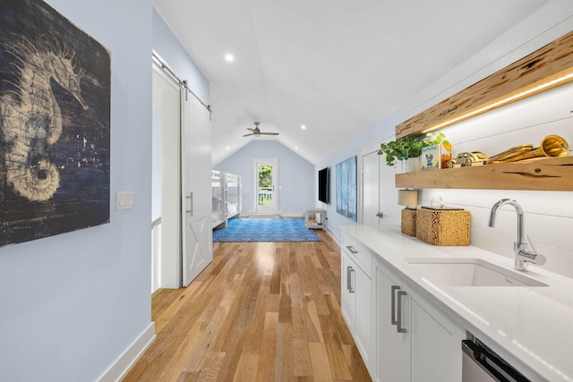 kitchen featuring white cabinets, light hardwood / wood-style floors, sink, a barn door, and vaulted ceiling