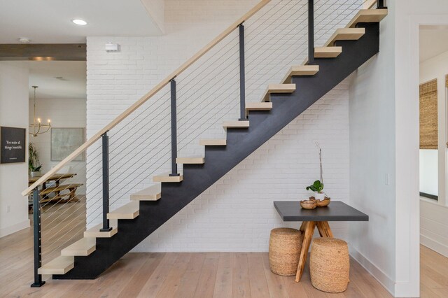 stairway featuring hardwood / wood-style floors, a chandelier, and brick wall