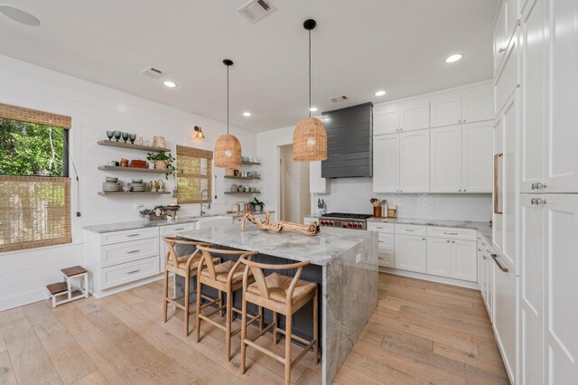 kitchen featuring light stone counters, light hardwood / wood-style floors, a center island, white cabinetry, and a kitchen breakfast bar