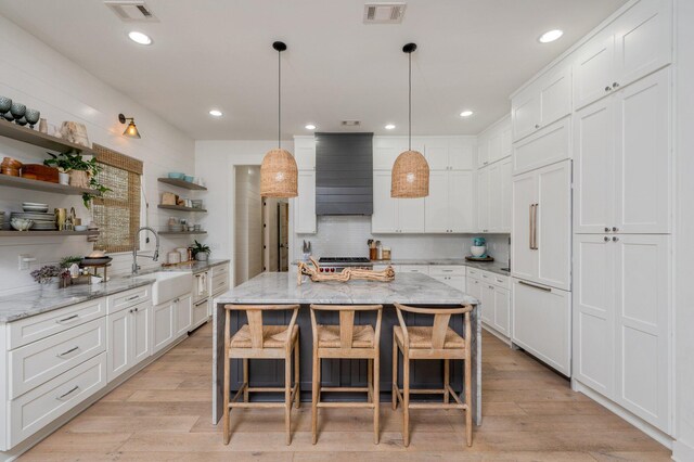 kitchen with white cabinets, sink, a kitchen island, light hardwood / wood-style flooring, and paneled fridge