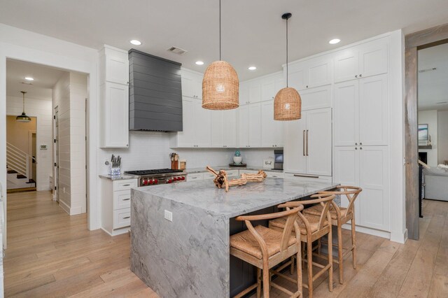 kitchen with a kitchen island, light stone countertops, light hardwood / wood-style flooring, and white cabinetry