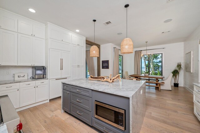 kitchen featuring white cabinets, built in appliances, light wood-type flooring, and hanging light fixtures