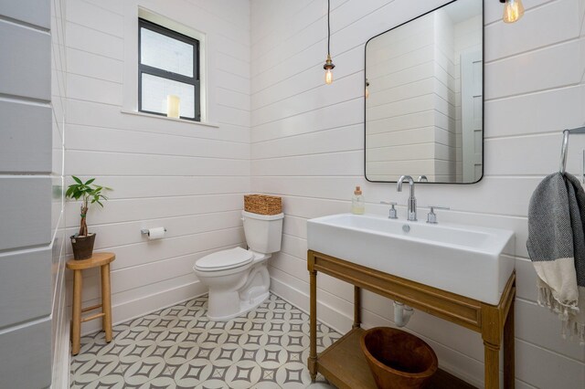 bathroom with wood walls, sink, and toilet