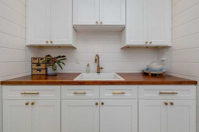 kitchen featuring wooden walls, butcher block countertops, sink, and white cabinets