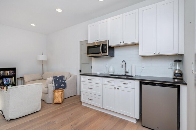 kitchen featuring tasteful backsplash, sink, white cabinetry, light hardwood / wood-style flooring, and appliances with stainless steel finishes