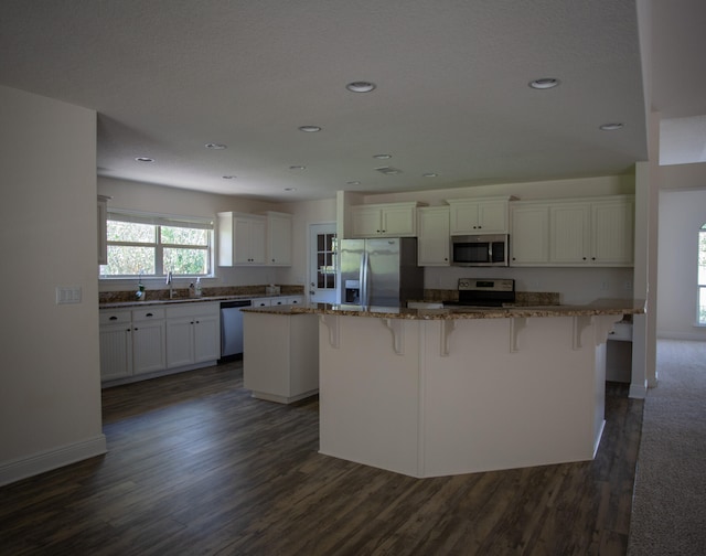 kitchen with stainless steel appliances, white cabinetry, sink, dark hardwood / wood-style floors, and a center island