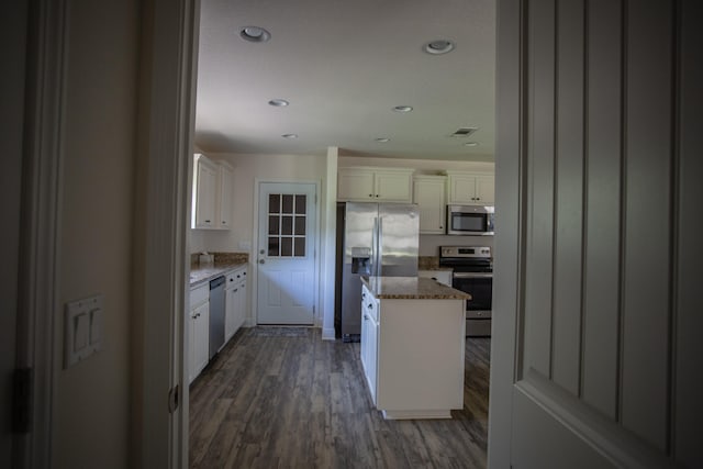 kitchen with stainless steel appliances, dark hardwood / wood-style flooring, light stone countertops, white cabinets, and a center island