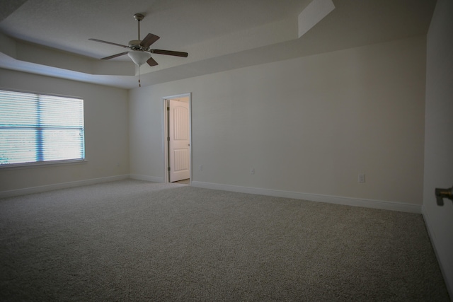 spare room with a tray ceiling, light colored carpet, and ceiling fan