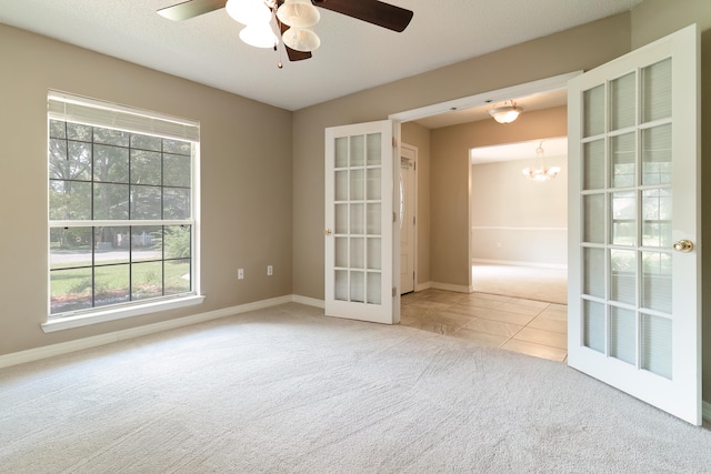 carpeted empty room featuring french doors, ceiling fan with notable chandelier, and a textured ceiling