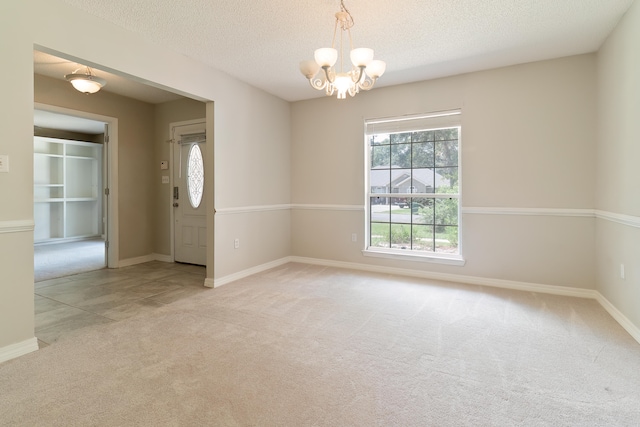 spare room featuring light colored carpet, a textured ceiling, and a notable chandelier