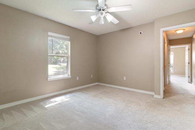 spare room with a textured ceiling, light colored carpet, and ceiling fan