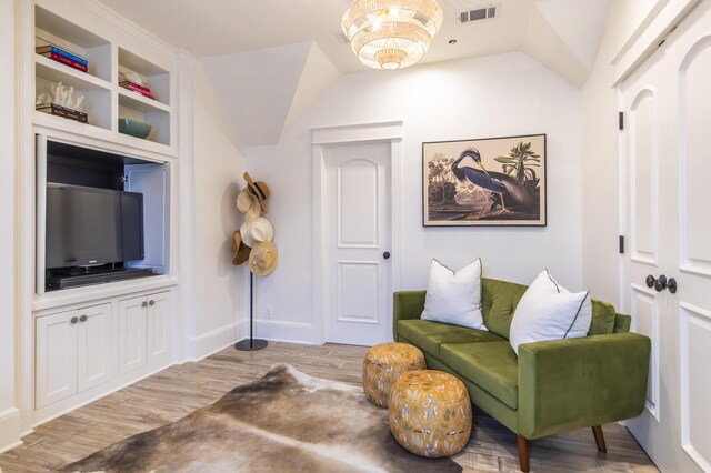 living area with a notable chandelier, lofted ceiling, and light hardwood / wood-style floors