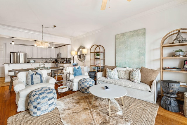 living room with ceiling fan with notable chandelier, light hardwood / wood-style flooring, and crown molding