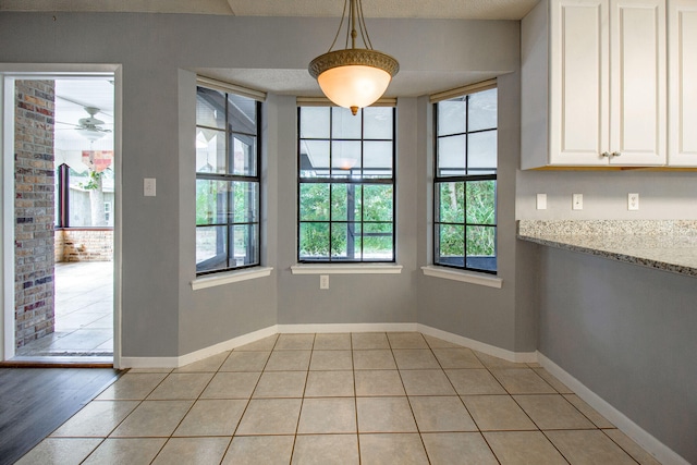 unfurnished dining area with ceiling fan, light tile patterned floors, brick wall, and a textured ceiling