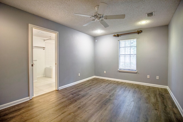 unfurnished bedroom featuring ceiling fan, a spacious closet, a textured ceiling, and hardwood / wood-style flooring