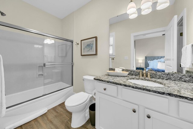 full bathroom with hardwood / wood-style floors, bath / shower combo with glass door, vanity, and toilet