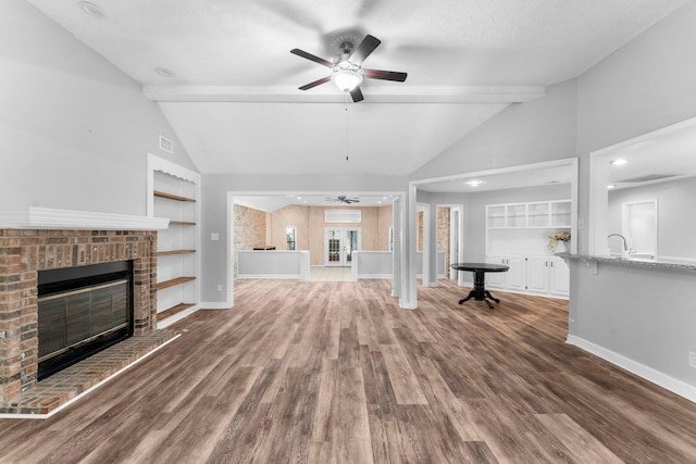 unfurnished living room featuring wood-type flooring, a fireplace, lofted ceiling with beams, and ceiling fan