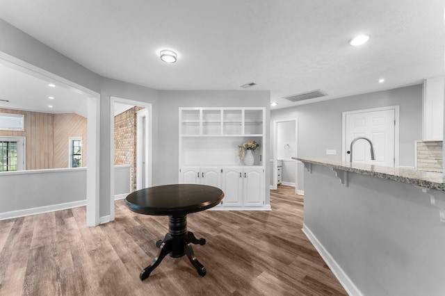 interior space with a textured ceiling, white cabinetry, light stone countertops, and hardwood / wood-style flooring