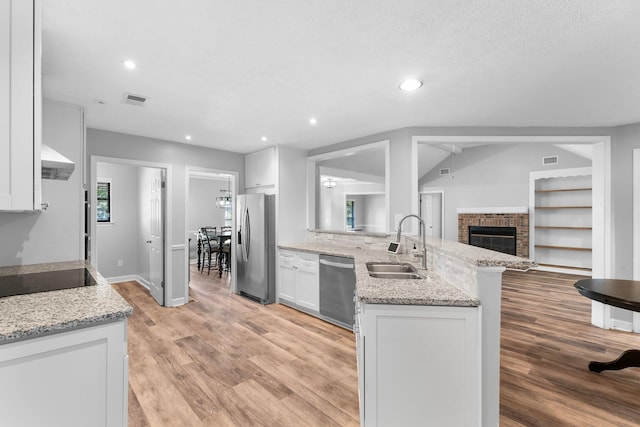 kitchen with white cabinetry, light stone counters, kitchen peninsula, stainless steel appliances, and sink