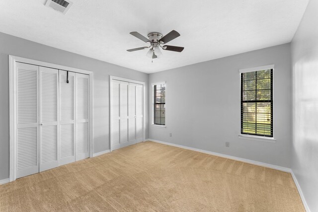 unfurnished bedroom featuring light carpet, multiple closets, and ceiling fan