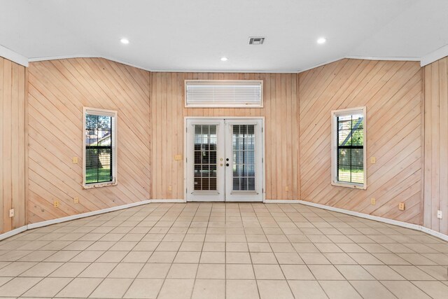 empty room with french doors, vaulted ceiling, wood walls, and light tile patterned floors