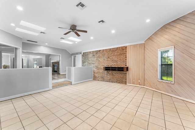 unfurnished living room with ceiling fan, light tile patterned flooring, wooden walls, and lofted ceiling with skylight