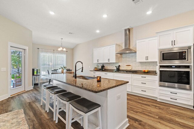 kitchen with sink, white cabinets, wall chimney range hood, a center island with sink, and appliances with stainless steel finishes