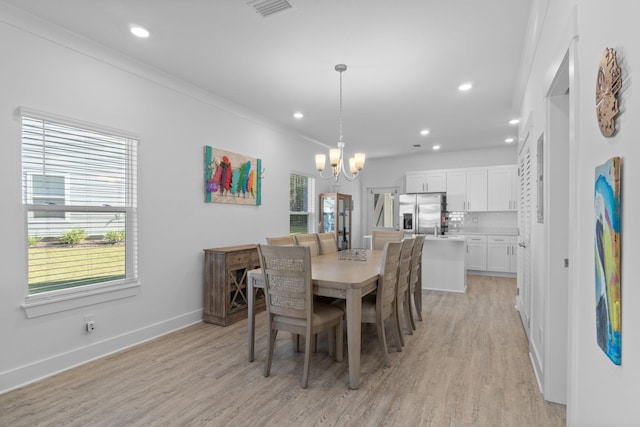 dining space with light hardwood / wood-style flooring, a wealth of natural light, crown molding, and a notable chandelier