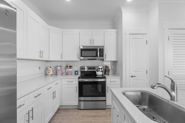 kitchen with sink, light hardwood / wood-style floors, light stone counters, white cabinetry, and stainless steel appliances