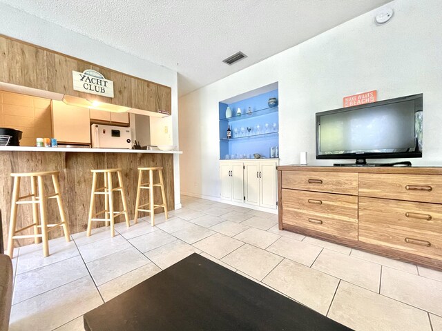 kitchen with visible vents, built in shelves, a textured ceiling, fridge, and a kitchen bar