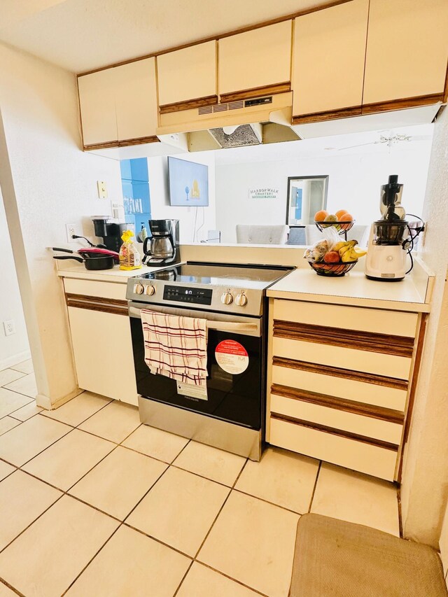 kitchen featuring light tile patterned floors, white cabinets, under cabinet range hood, light countertops, and stainless steel range with electric stovetop