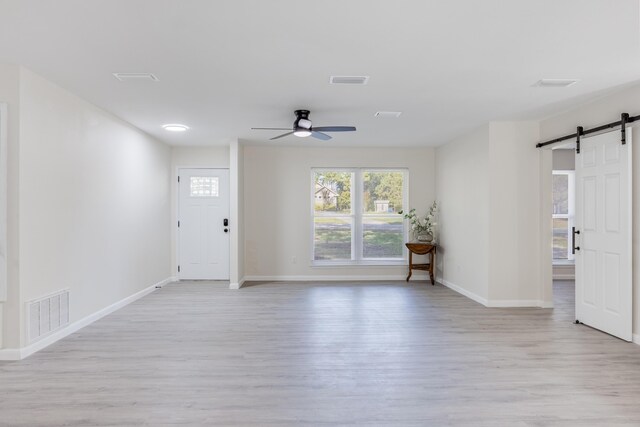 spare room with ceiling fan, light hardwood / wood-style flooring, and a barn door