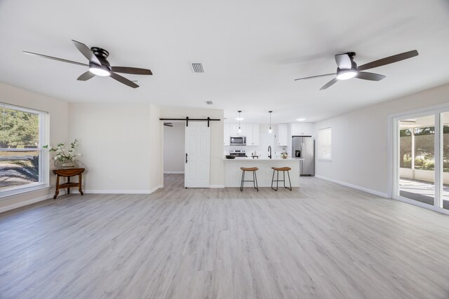 unfurnished living room featuring a barn door, light wood-type flooring, sink, and ceiling fan