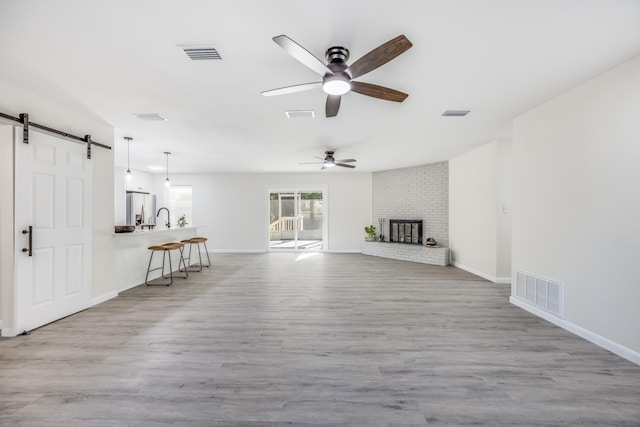 unfurnished living room featuring a brick fireplace, light hardwood / wood-style floors, ceiling fan, and a barn door