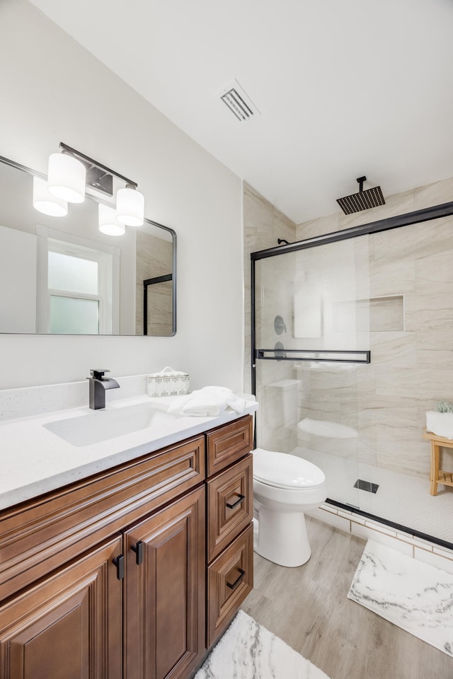 bathroom featuring hardwood / wood-style floors, a shower with shower door, vanity, and toilet