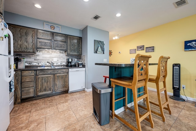 kitchen featuring dark brown cabinetry, light tile patterned flooring, sink, white appliances, and decorative backsplash