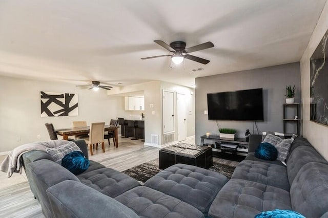 living room featuring baseboards, visible vents, ceiling fan, and light wood finished floors