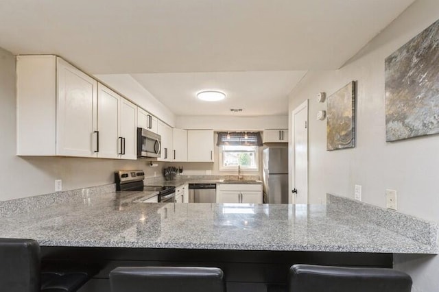 kitchen with a peninsula, appliances with stainless steel finishes, a sink, and white cabinetry